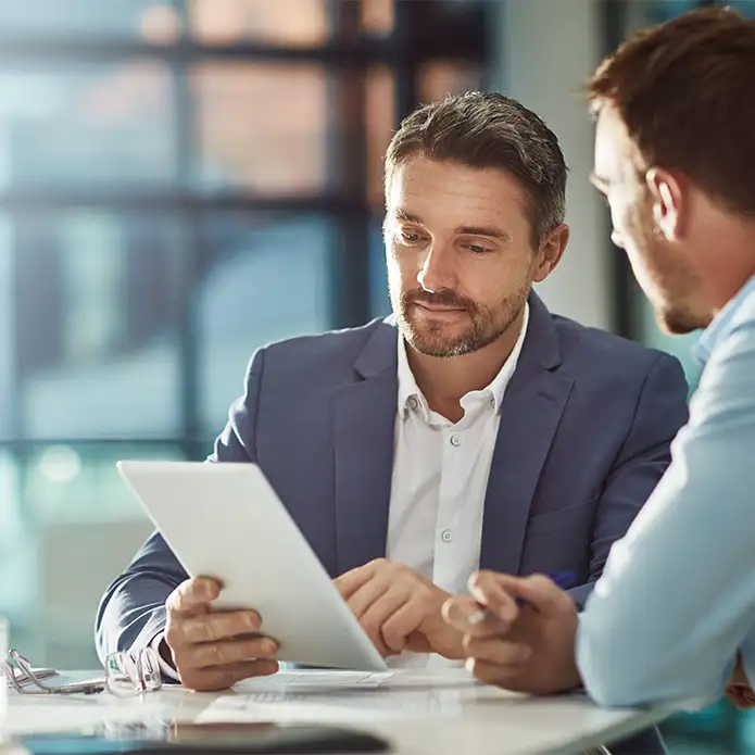 Zwei IT-Freelancer sitzen an einem Tisch und schauen gemeinsam auf ein Tablet.