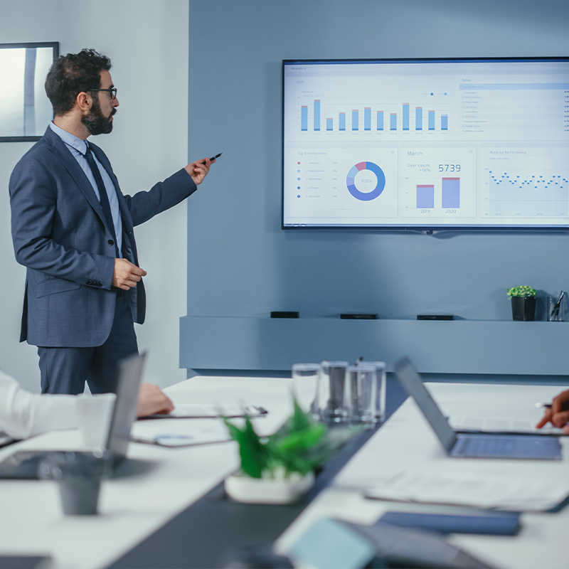 Geschäftsmann präsentiert Diagramme und Daten auf einem Bildschirm während eines Meetings.